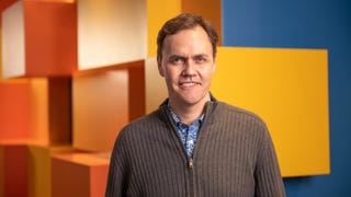 Picture of Schell Games CEO Jesse Schell looking at the camera and smiling. He is standing in front of an orange, yellow, and blue wall with a geometric design